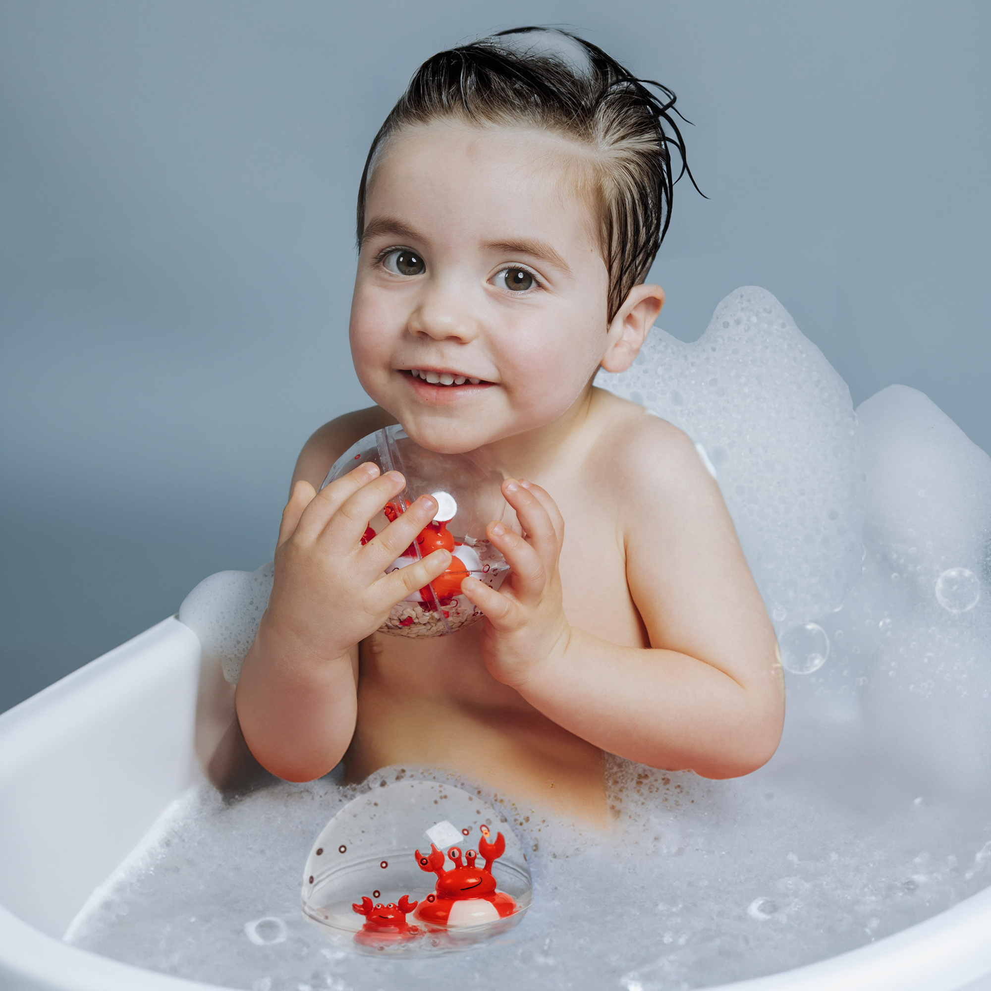 Bébé jouant avec la balle sensorielle Petit Boum Happy Bubbles pendant le bain